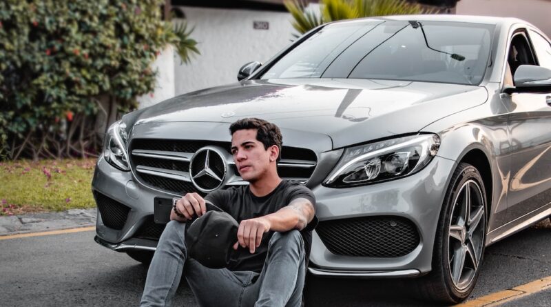 unknown celebrity sitting siting beside silver Mercedes-Benz car outdoors