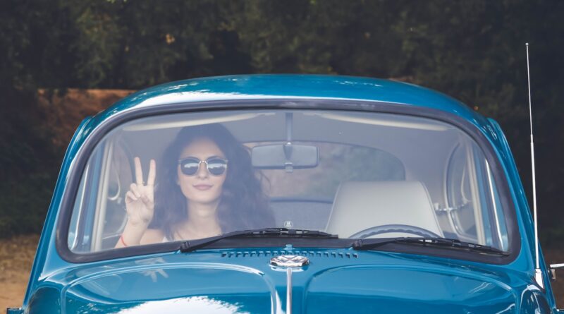 woman sitting in passengers seat of blue Volkswagen Beetle and performing peace sign